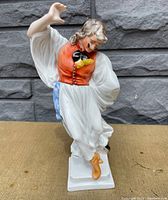 Front view of the porcelain figurine showing the man in mid-dance pose with orange vest and white clothing.