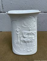 Front view of white porcelain vase showing embossed lady reclining on bench in garden scene with flowers and urn on pedestal