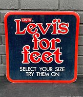 Front view of vintage Levi's metal store display sign with navy background and red border, promoting Levi's denim shoes.