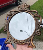 Front view of the ornate vintage circular mirror showing detailed gold-toned frame with Rococo/Baroque inspired floral and scroll motifs.
