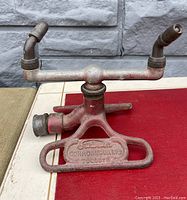 Front view of the vintage Rain King Model 6 lawn sprinkler showing cast iron base with worn red paint, stamped lettering and brass nozzle arms.
