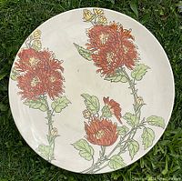 Top-down view of beige ceramic plate with orange chrysanthemum flowers and green leaves pattern on a grass background