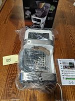 New sealed Braun BrewSense KF 6050 coffee maker in plastic wrap with carafe and manual beside it, displayed on wood floor.