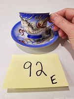 Photo of the tea cup and saucer showing hand holding the tea cup to reveal raised dragon detail and cobalt blue color with gold accents.