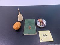 The lot composed of four items: orange darning egg, small white oiler, Singer sewing machine instruction manual in green cover, round tin with bobbins and small accessories