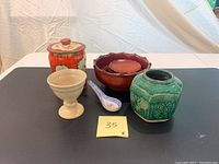 Photo of lot showing wood bowl with three side plates, vintage tin, green pottery chalice vase, ceramic chalice bowl, and ceramic spoon.