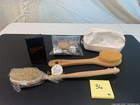 Full lot showing two dry brushes, Azzaro cologne, white toiletry bag, and small bag of hair clips on table.