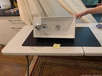White rectangular vessel sink with chrome faucet mounted on left side on a table indoors.
