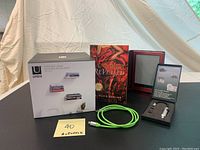 Sony PRS-650 e-reader next to novel, Umbra book shelves box, boxed reading light and green charging cable