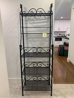 Full view of black cast iron bakers rack with multiple shelves and scrollwork design.