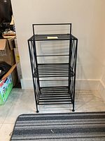 Front view of the black cast iron foldable plant stand showing three slatted shelves and straight sides with round foot caps.