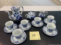 Full set of Delft Blue tea service laid out: 6 teacups with saucers, sugar dish, creamer, and teapot on black cloth.