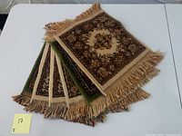 Set of six wool placemats stacked showing fringed edges and patterned designs in shades of brown and beige, with one green placemat visible.