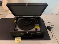 Open suitcase record player top view with record player platter and tonearm, latch and power cord visible.