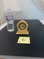 Full view of ivory alabaster clock placed next to water bottle for scale, showing overall shape and size.