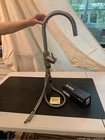 Grohe kitchen faucet with brushed nickel finish, high arc curved spout, single handle lever, and two braided supply hoses. A Kraus branded box is placed next to it on the table.