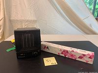 Honeywell heater and boxed Magnificent broom holder on a table with a beige backdrop.