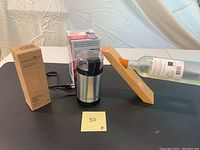 Photo of the Black and Decker coffee grinder in front of its original packaging, next to the wood wine holder with a bottle inserted for demonstration.