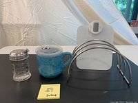 Photo of vintage sugar dispenser, blue ceramic soup warmer, stainless steel pot organizer, and white Lee Valley kitchen scale on black surface.