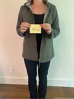 Front view of model wearing grey-black Novelti trench rain coat, holding a size card '87 E'.