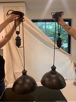 Photo of two black pulley ceiling lamps held up for viewing, showing full lamp bodies including pulley, cord, and dome shade.