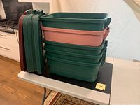 Five Plastic Rubbermaid storage containers, four green and one pink, stacked with lids and side handles visible.