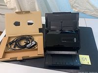 Black Fujitsu ScanSnap iX500 document scanner with input and output trays opened on black surface with cables in a cardboard tray beside it.