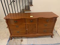 Full front view of solid oak dresser showing curved top, six drawers with metal handles and central cabinet door with carved design.