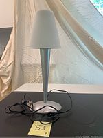Full view of the vintage Ikea table lamp with glass shade, showing the lamp standing on a black surface with a cream backdrop, black power cord visible.