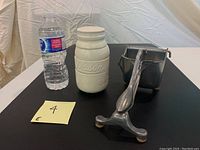 Photo showing the vintage aluminum citrus squeezer in front of the Mason jar container and water bottle for scale.