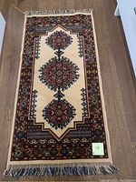 Full view of the wool table runner on the floor showing geometric diamond medallions, bordered pattern and fringes.