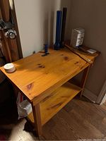 Smaller pine end table with natural finish, visible knots, two shelves, placed against wall with some items on top