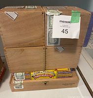 Photo showing four square wooden cigar boxes stacked with two rectangular branded cigar boxes beneath them, including Montecristo and Partagas boxes.