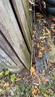 Stack of gray metal block lock panels leaning against wooden structure surrounded by dry leaves and debris