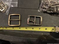 Photo showing two distinct rectangular metal buckles placed beside a measuring tape for size reference.