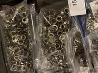 Mixed metal grommets in several clear plastic bags on a flat surface, suitable for leatherworking.