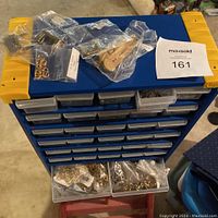 Blue plastic organizer cabinet with multiple small drawers and several plastic bags of hardware on top