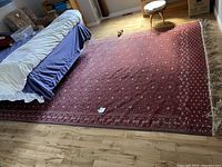 Entire red oriental rug laid on wood floor, showing pattern and fringe
