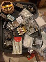 Various leatherworking accessories spread on a tray, showing multiple small items including an anvil, tins, and containers with metal hardware and tools.