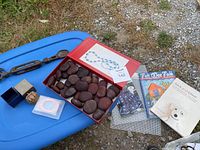 View of lot items arranged on blue surface including seed pods box, craft books, carved wooden lucky spoon, perfume box, bracelets and guitar string.
