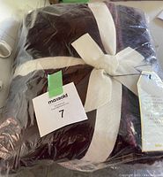 Packaged wine colour faux fur throw blanket tied with cream ribbon, plastic wrapped, showing brand tag.