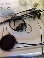 Photo showing microphone mounted on adjustable stand, pop filter attached, and black Bluetooth headphones lying on surface.