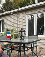 Photo of the small glass patio set including a square glass-top table and three matching green fabric chairs outdoors near a house with vinyl siding.