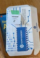 Closed white and blue SunFounder box with branded graphics and partial view of instructional book.