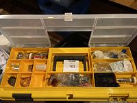 Top view of yellow tool kit compartment with assorted small metal hardware parts, clips, rings, and leatherworking accessories.