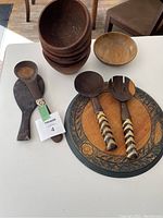 Photo showing stacked wooden bowls, wooden salad spoons with patterned handles, and a large round wooden bread board with carved decorative border.