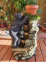 Front and side views of the bear water fountain showing detailed bear sculpture climbing rocky textured fountain with terracotta flower pot and faux moss.
