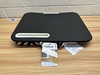 Front top view showing black lap desk with phone holder slot and visible rip on surface, product tags attached.