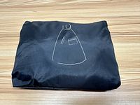 Folded black rain poncho with white illustration of a poncho showing an opening and a pocket.
