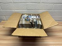 Large cardboard box filled with stacks of baseball cards and loose cards on top.